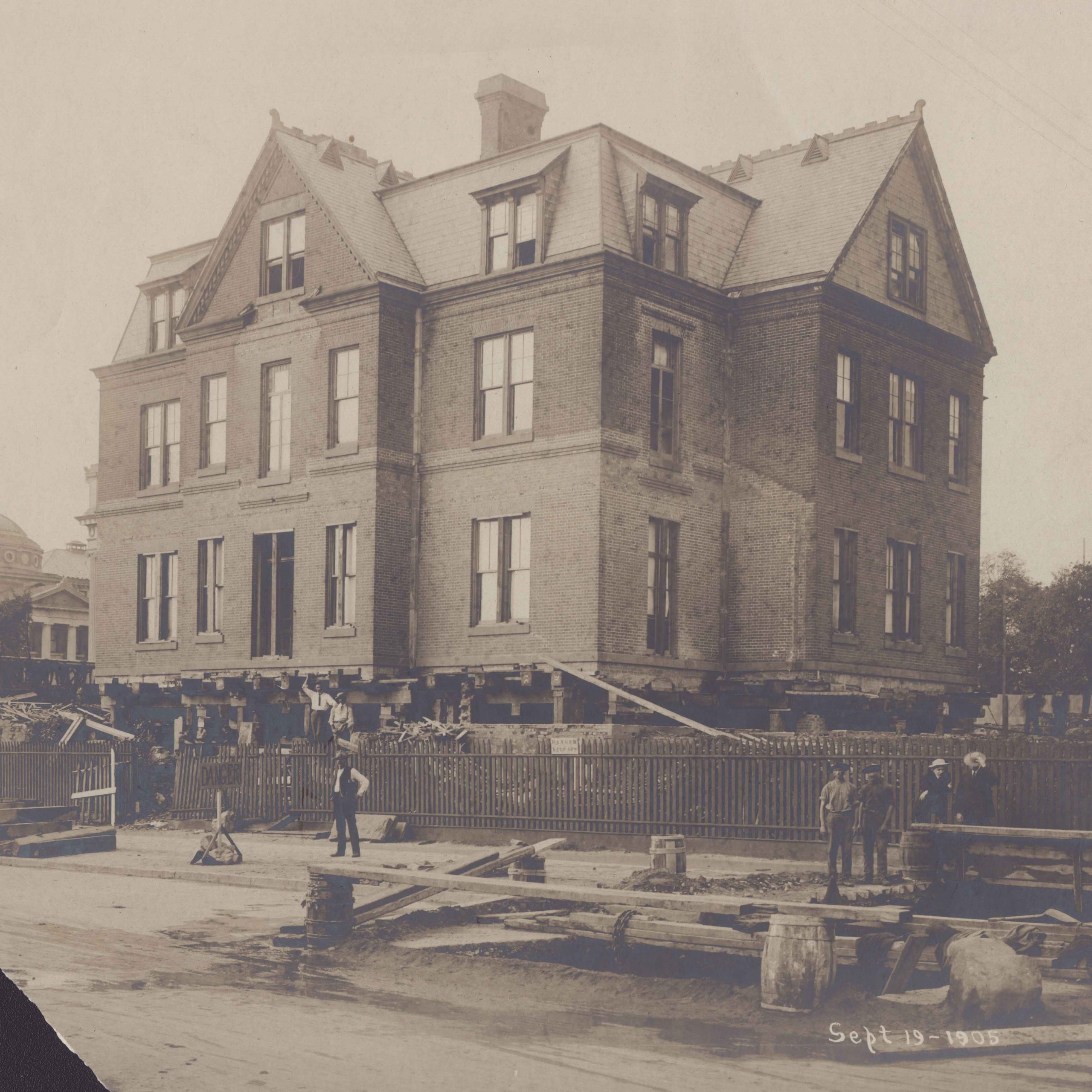 Buell Hall, a small, domestic in appearance 3 story building, is lifted up on wood in preparation for a move.